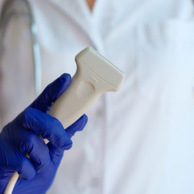 Close-up of a doctor in a white coat and blue gloves holding a doppler ultrasound probe