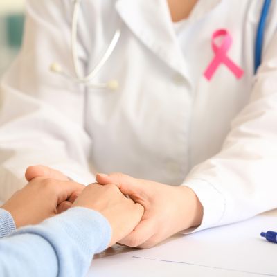 Doctor with a pink ribbon for breast cancer awareness holding their patient's hands